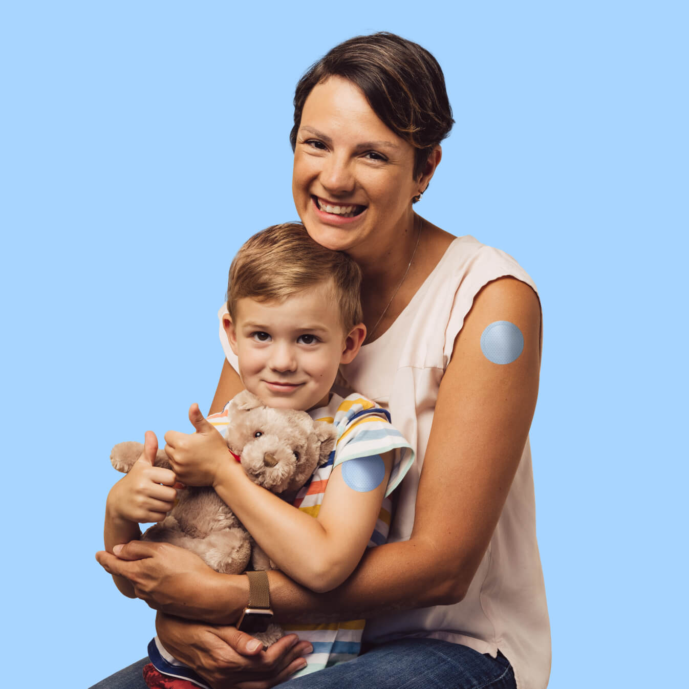 Mother and child smiling while holding a teddy bear, showcasing a comfortable Prepare patch on the child's arm.